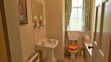 Un baño con lavamanos, inodoro y ventana con cortinas.