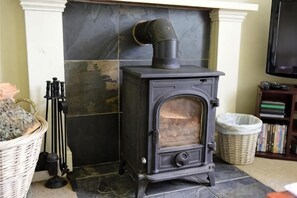 A black wood-burning stove with a chimney, a wicker basket, and a fireplace mantel. - Gardener's Cottage, Glen Lyon (Aberfeldy)