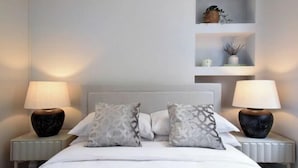 A neatly made bed with two pillows, two bedside lamps, and a shelf with decorative items above the bed.