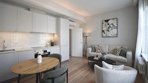 A modern kitchen with white cabinets, a dining table with chairs, a sofa, and a floor lamp.