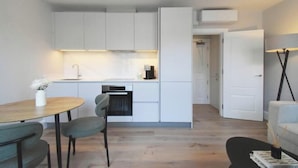 A compact kitchen with white cabinets, a dining table with chairs, and a sofa in a modern living area.