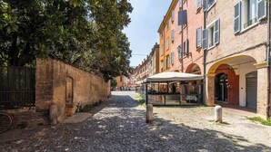 A cobblestone street with a covered outdoor seating area, brick buildings, and a metal fence. - Suite Modena al Centro - Affitti Brevi Italia (Modena)