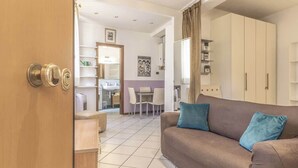 A modern living room with a sofa, a dining area with chairs, and a kitchen visible through an open door. - MonoliVi 35 - Affitti Brevi Italia (Modena)