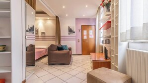 A modern hotel room with a sofa, a small table, and a radiator. There is a door with a sign on it, and a shelf with items on the wall. - MonoliVi 35 - Affitti Brevi Italia (Modena)