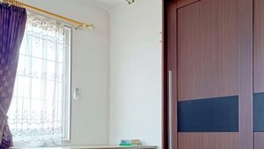 Una habitación con un armario de madera, una ventana con cortina y un escritorio con silla.