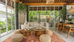 A modern living room with a sofa, two round coffee tables, and a dining table with chairs. - Villa Nana by Pertama Stay (Bali)