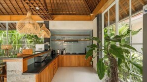 A modern kitchen with wooden cabinets, a black countertop, and hanging wicker lights. - Villa Nana by Pertama Stay (Bali)