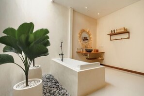 A modern bathroom with a freestanding bathtub, a large mirror, and a wooden shelf. - Villa Nana by Pertama Stay (Bali)