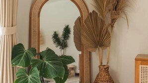 A room with a rattan-framed mirror, a wooden cabinet, and a large green plant. - Villa Nana by Pertama Stay (Bali)