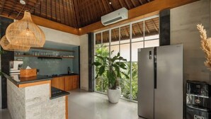 A modern kitchen with a stone island, stainless steel appliances, and a large window with a view of greenery. - Villa Nana by Pertama Stay (Bali)