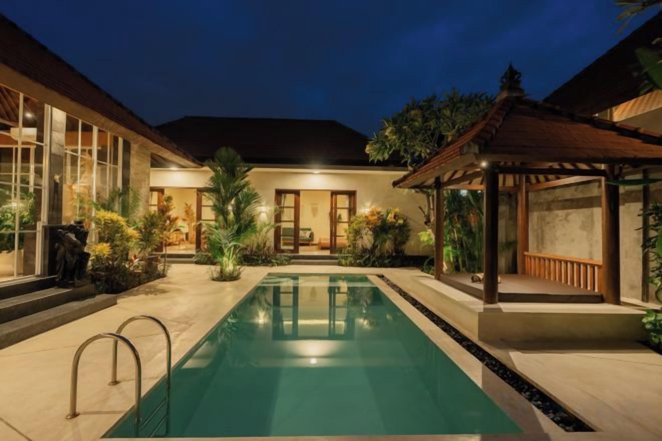 A swimming pool with a pergola, a covered seating area, and a building with large windows.