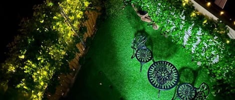 Un espace extérieur aménagé avec des tables et des chaises, entouré de verdure et illuminé par des guirlandes lumineuses.