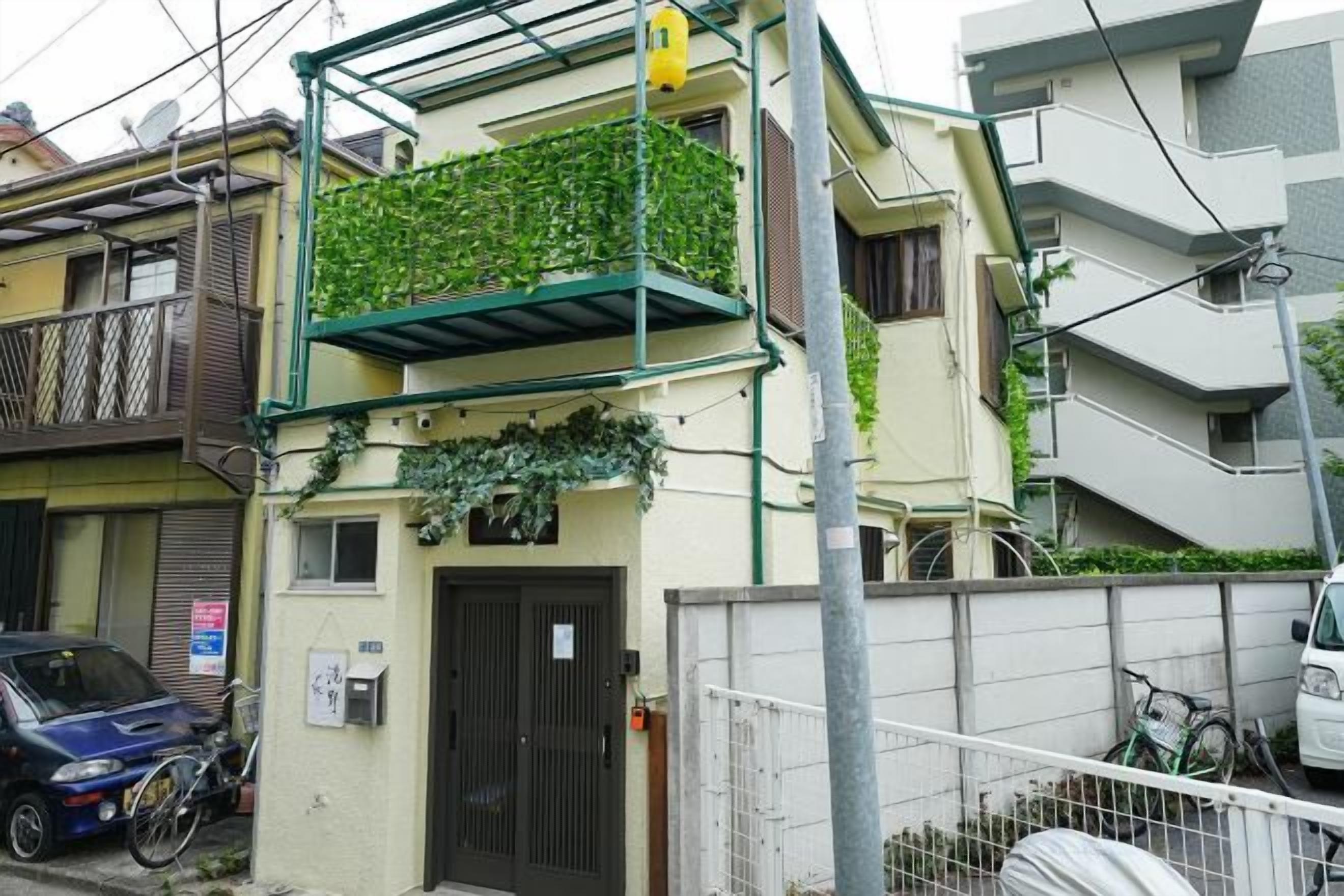 A residential building with a balcony covered in greenery, a gated entrance, and a parked car.
