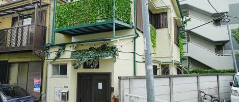 A residential building with a balcony covered in greenery, a gated entrance, and a parked car.