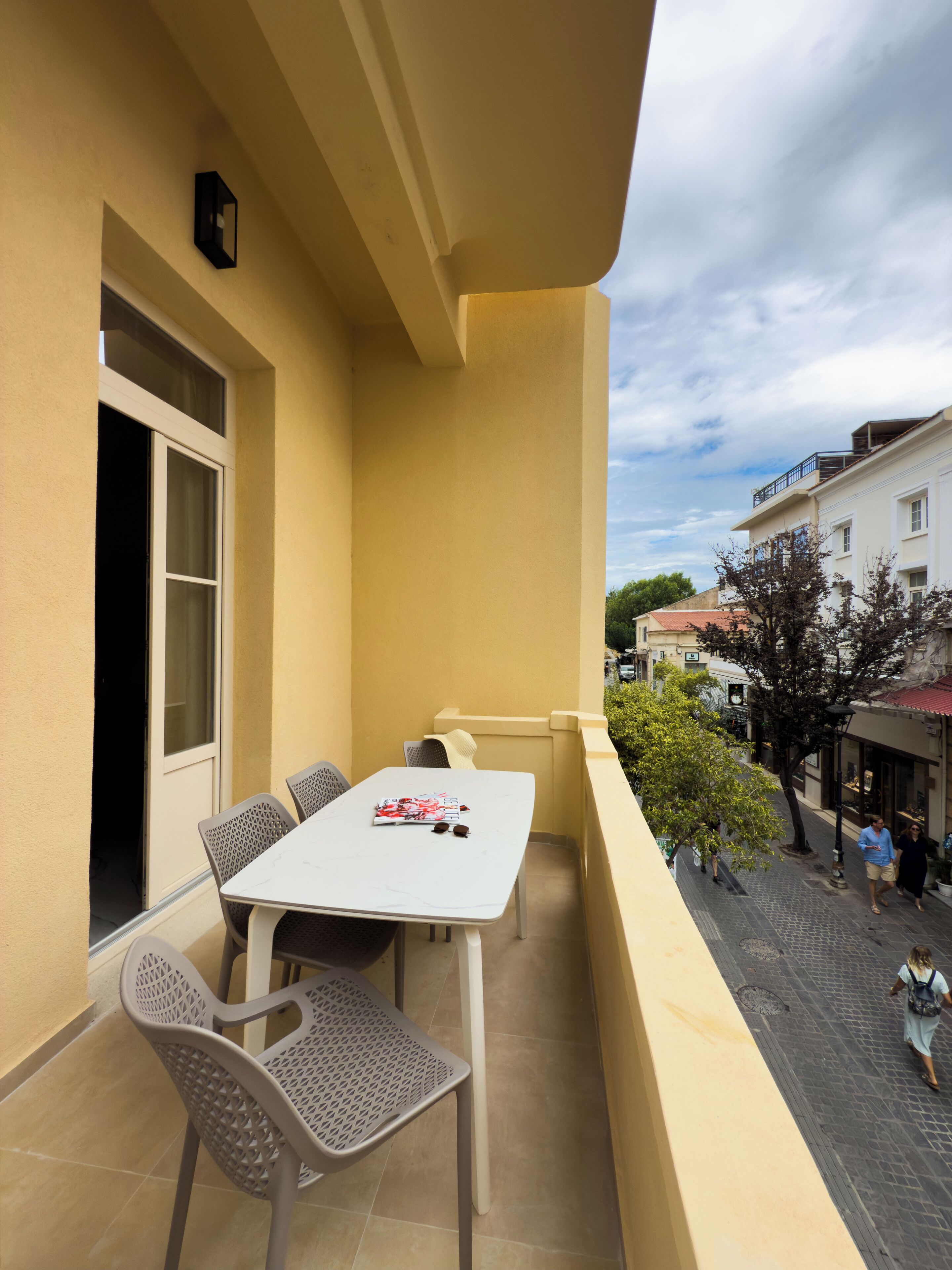 A balcony with a table and chairs, a window, and a view of the street below.