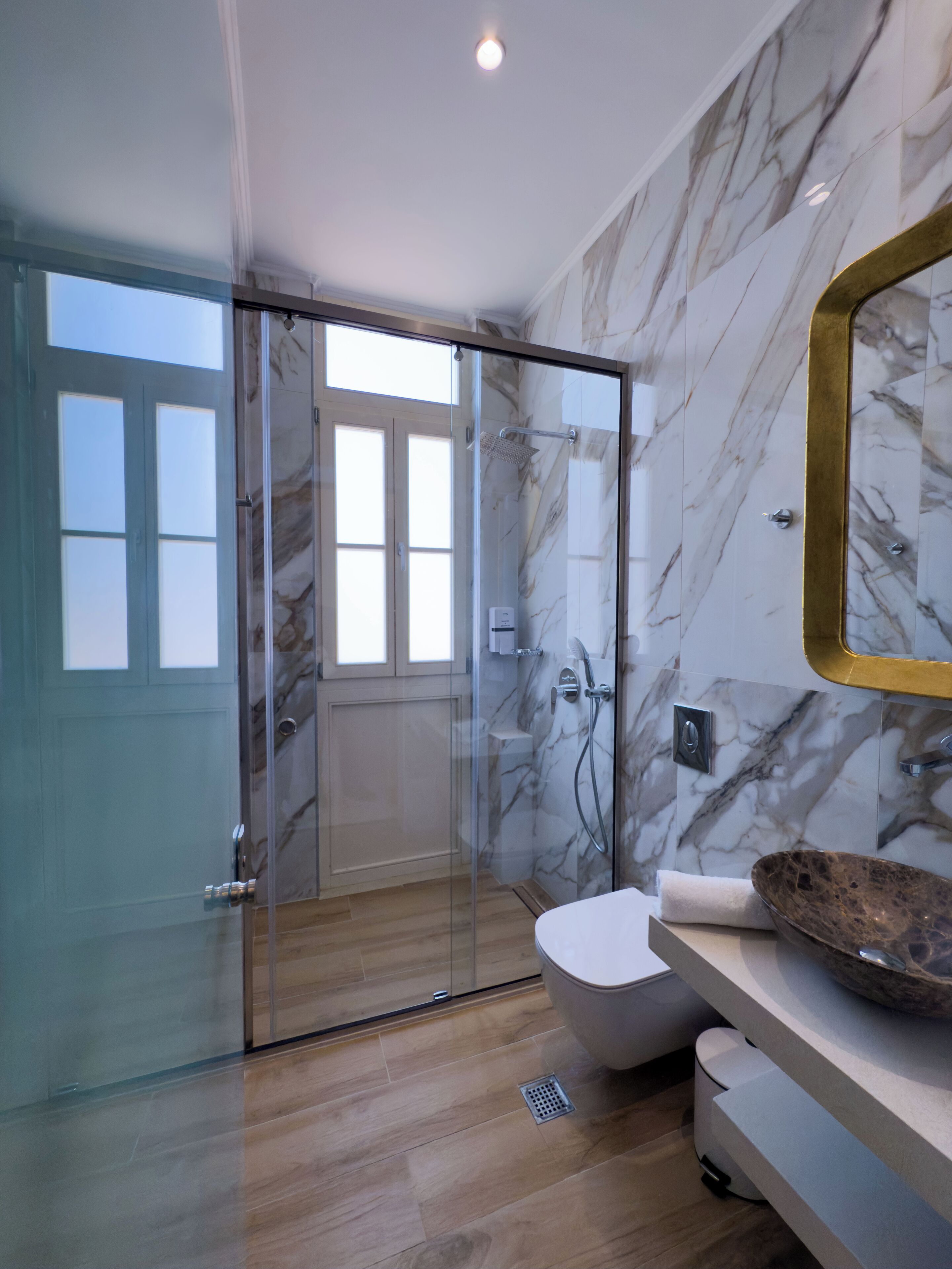 A modern bathroom with a glass-enclosed shower, marble walls, and a large mirror.