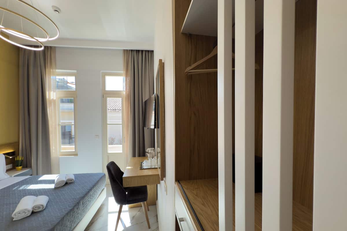 A modern hotel room with a bed, a desk, a chair, a TV, and a wardrobe.