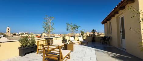 Una terraza en la azotea con un banco de madera, plantas en macetas y vistas de la ciudad.