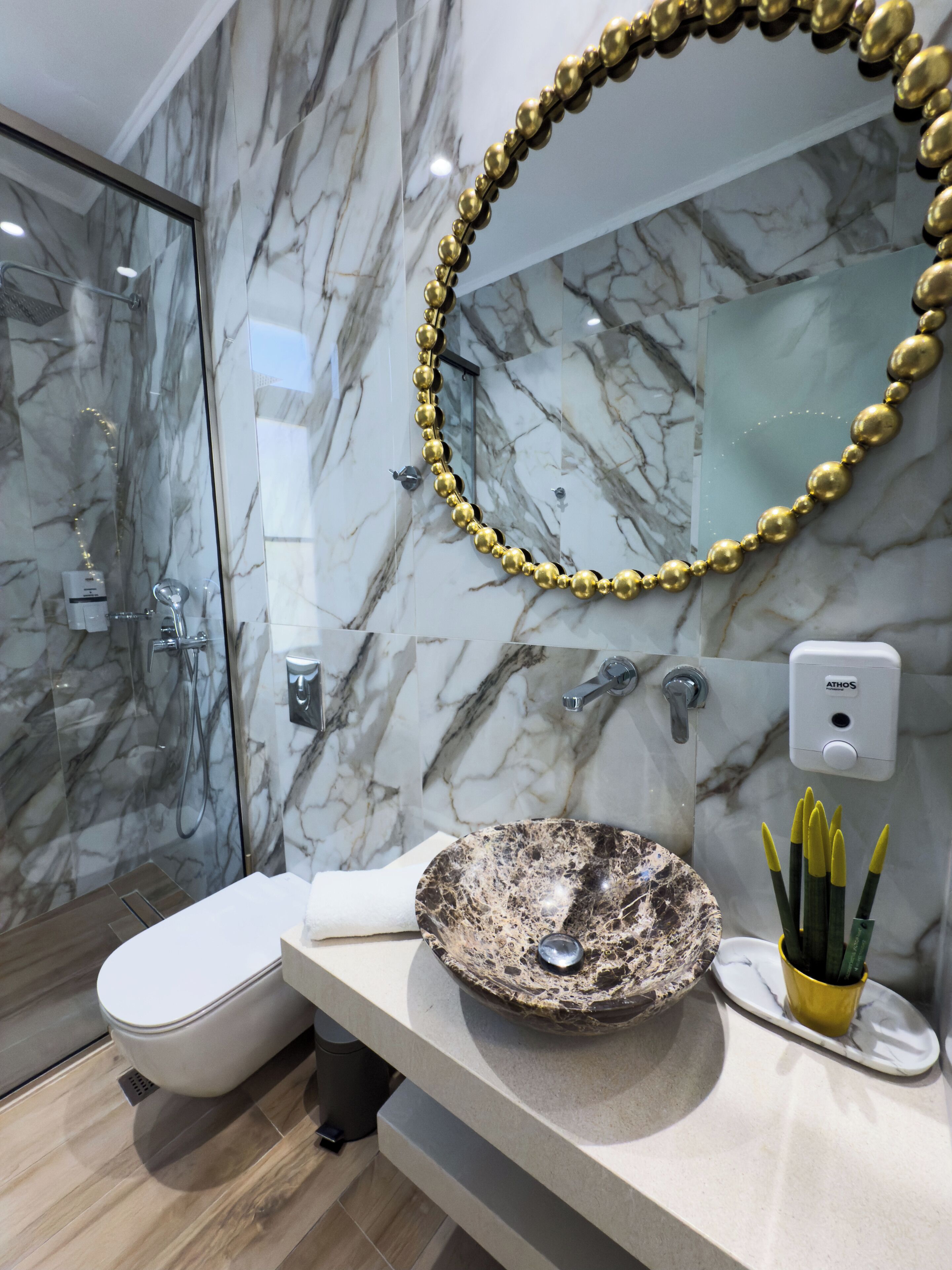 Une salle de bain moderne avec une douche à parois de verre, un lavabo en marbre et un collier de perles dorées accroché au mur.