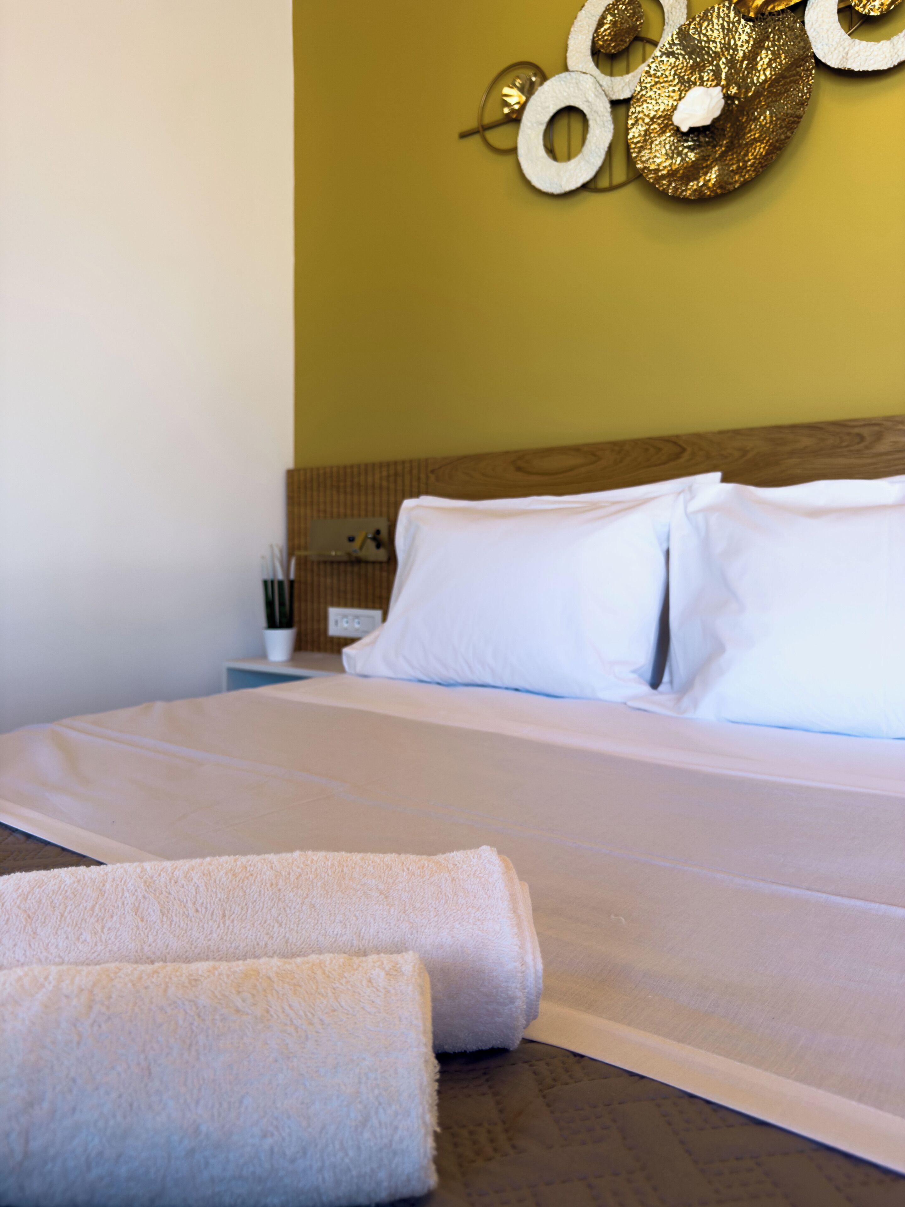 A neatly made bed with white linens, a wooden headboard, and a wall with a decorative gold and white circular design.
