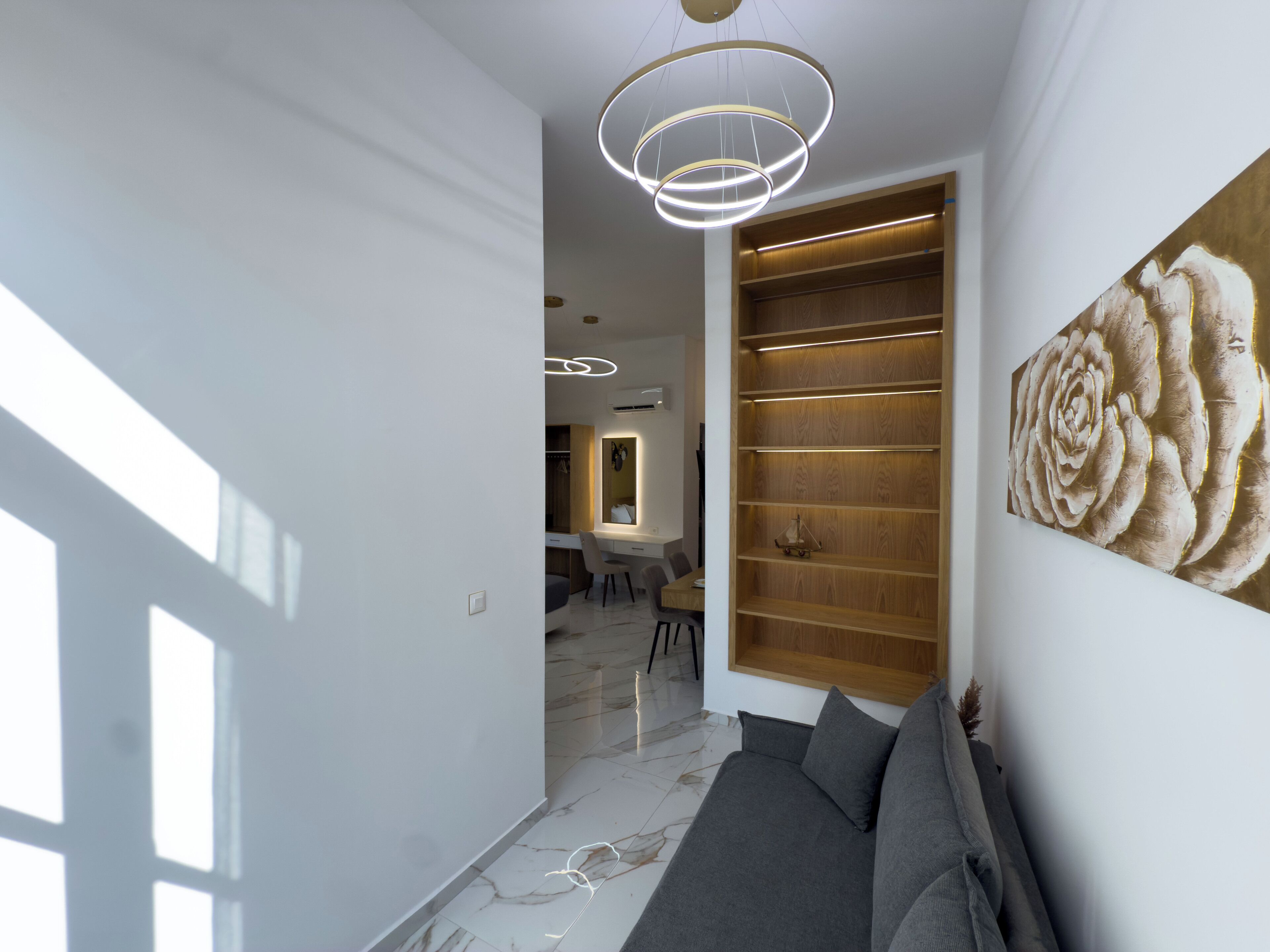 Ein modernes Interieur mit Marmorboden, einem grauen Sofa, Holzregalen und einem großen floralen Kunstwerk.