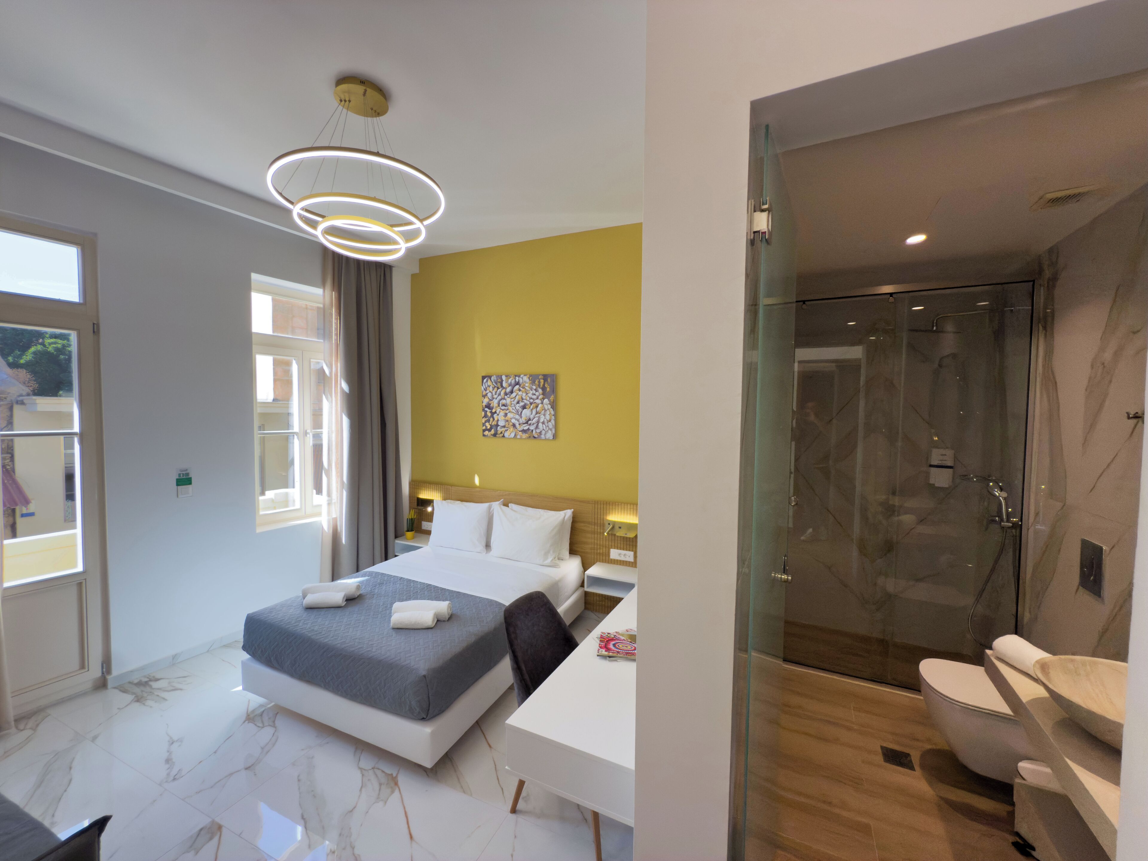 A modern hotel room with a large bed, a glass-enclosed shower, and a white bathroom.