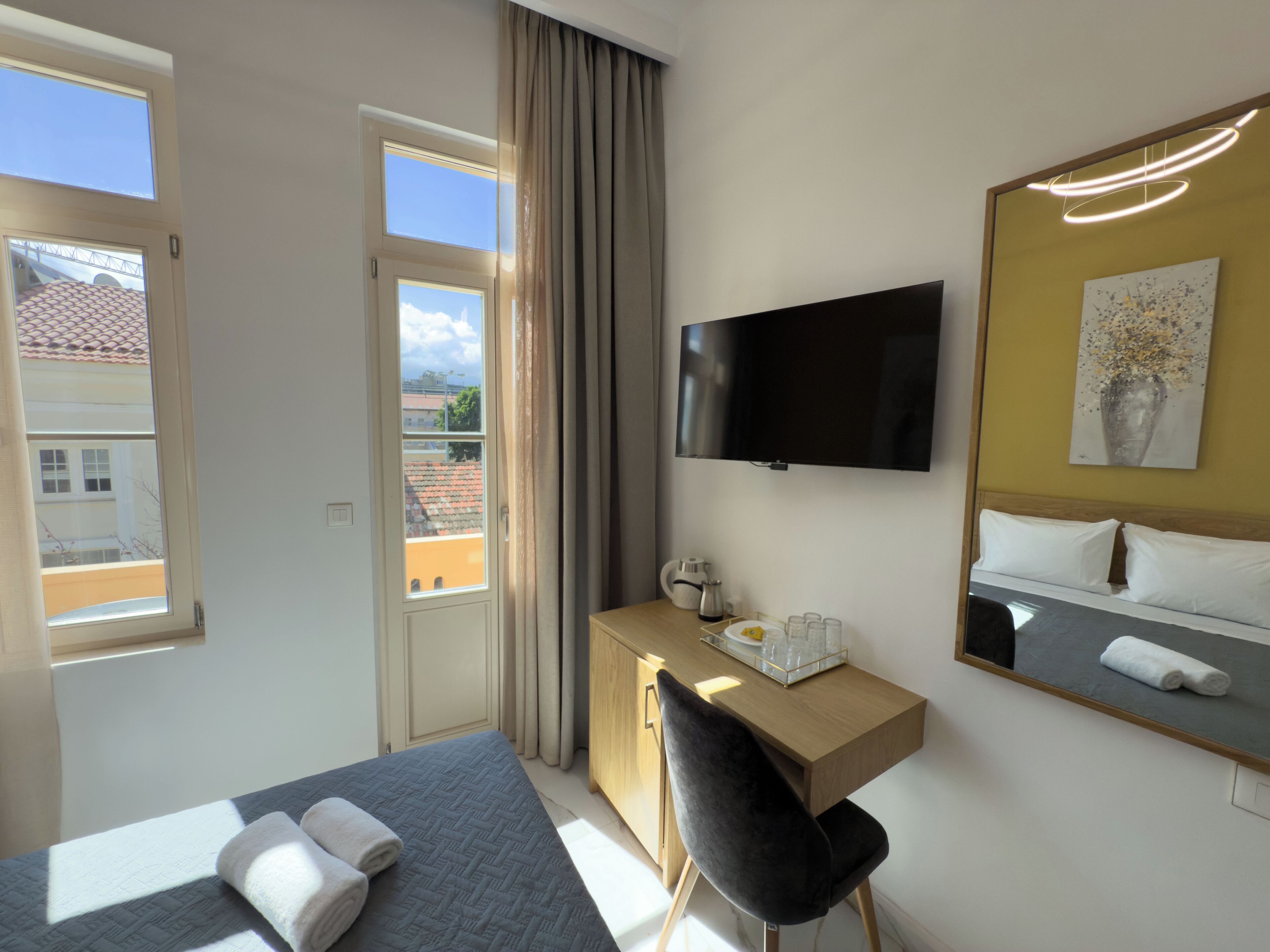 A hotel room with a bed, a desk with a chair, a television, and a window with curtains.
