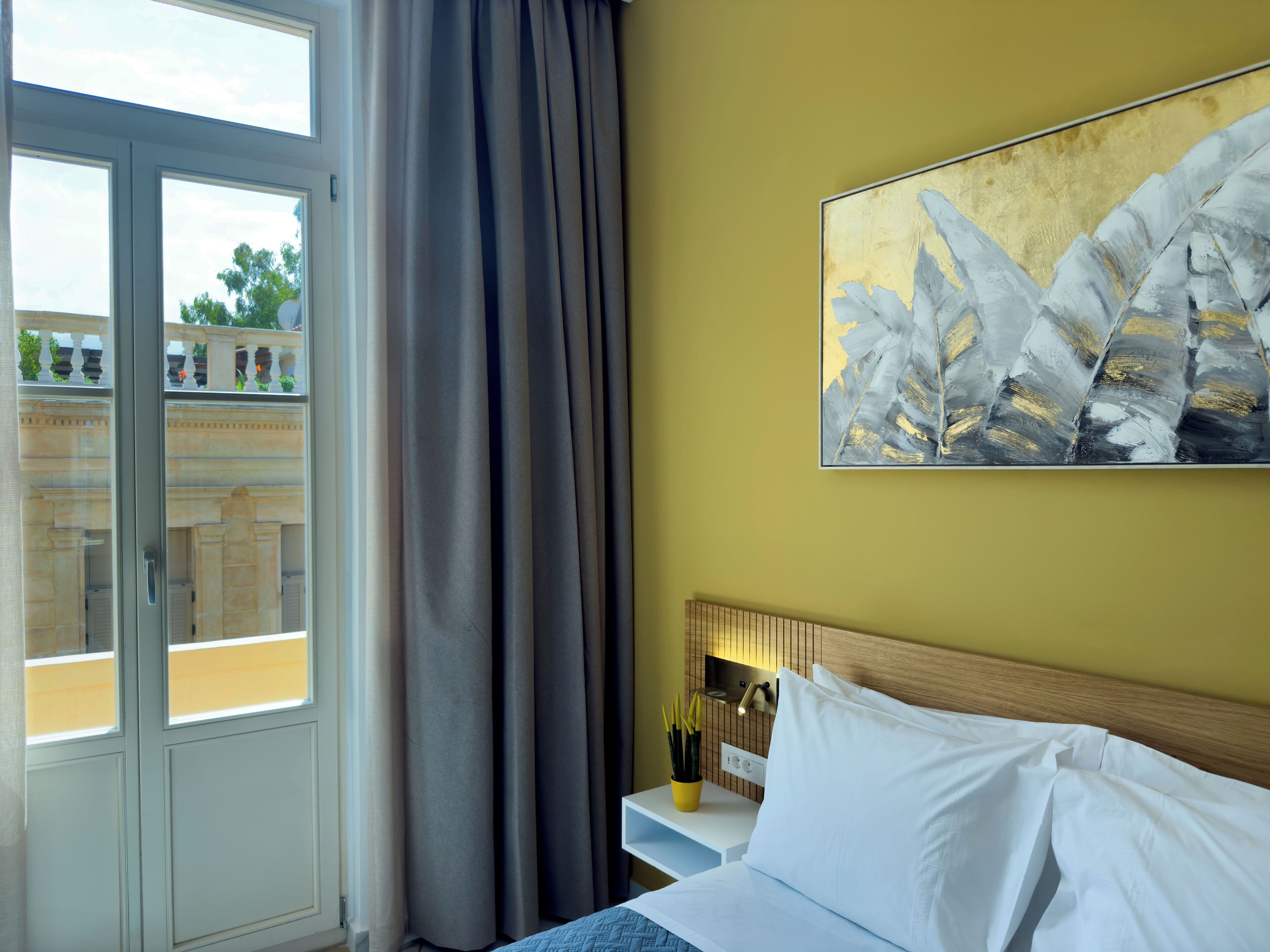 Une chambre d’hôtel avec un lit, une table de chevet, un tableau et une fenêtre avec des rideaux.