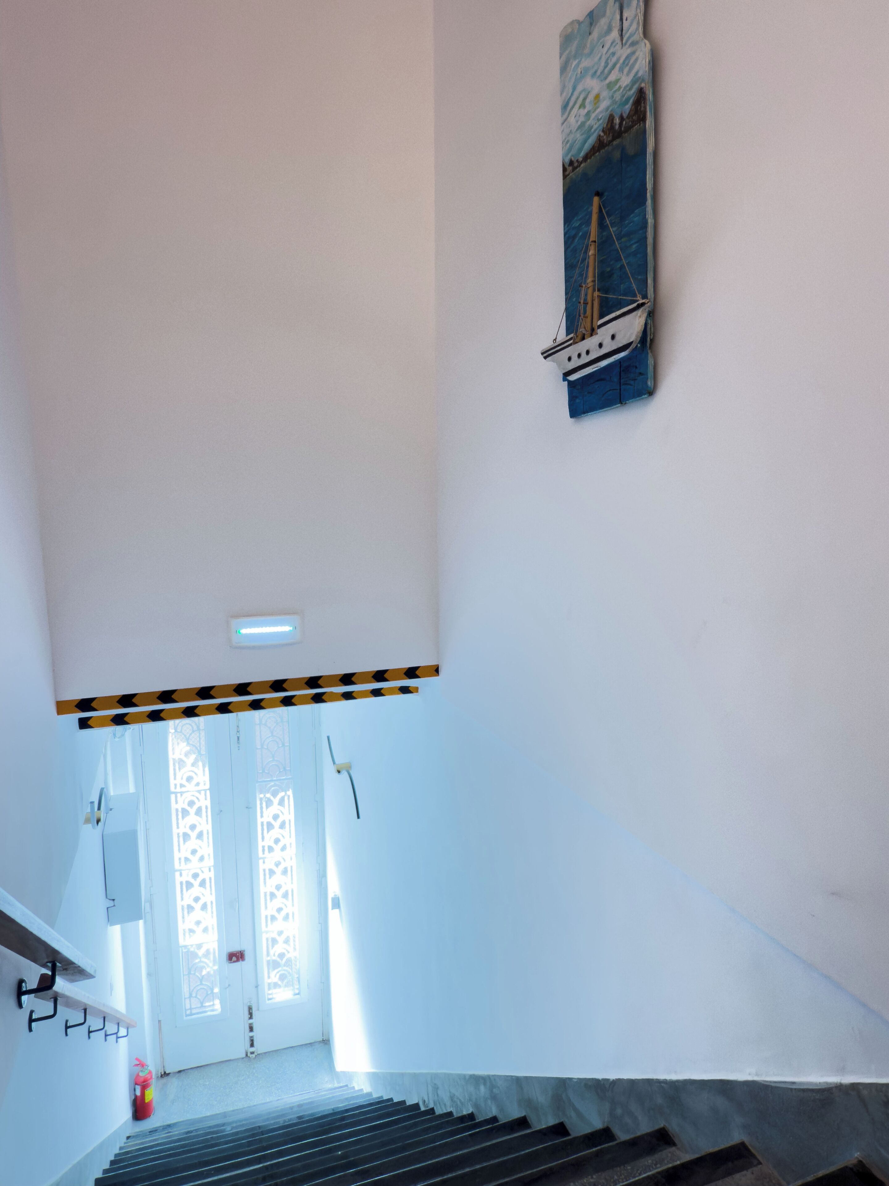 Una escalera con barandilla, un extintor y una puerta con paneles de vidrio decorativos.