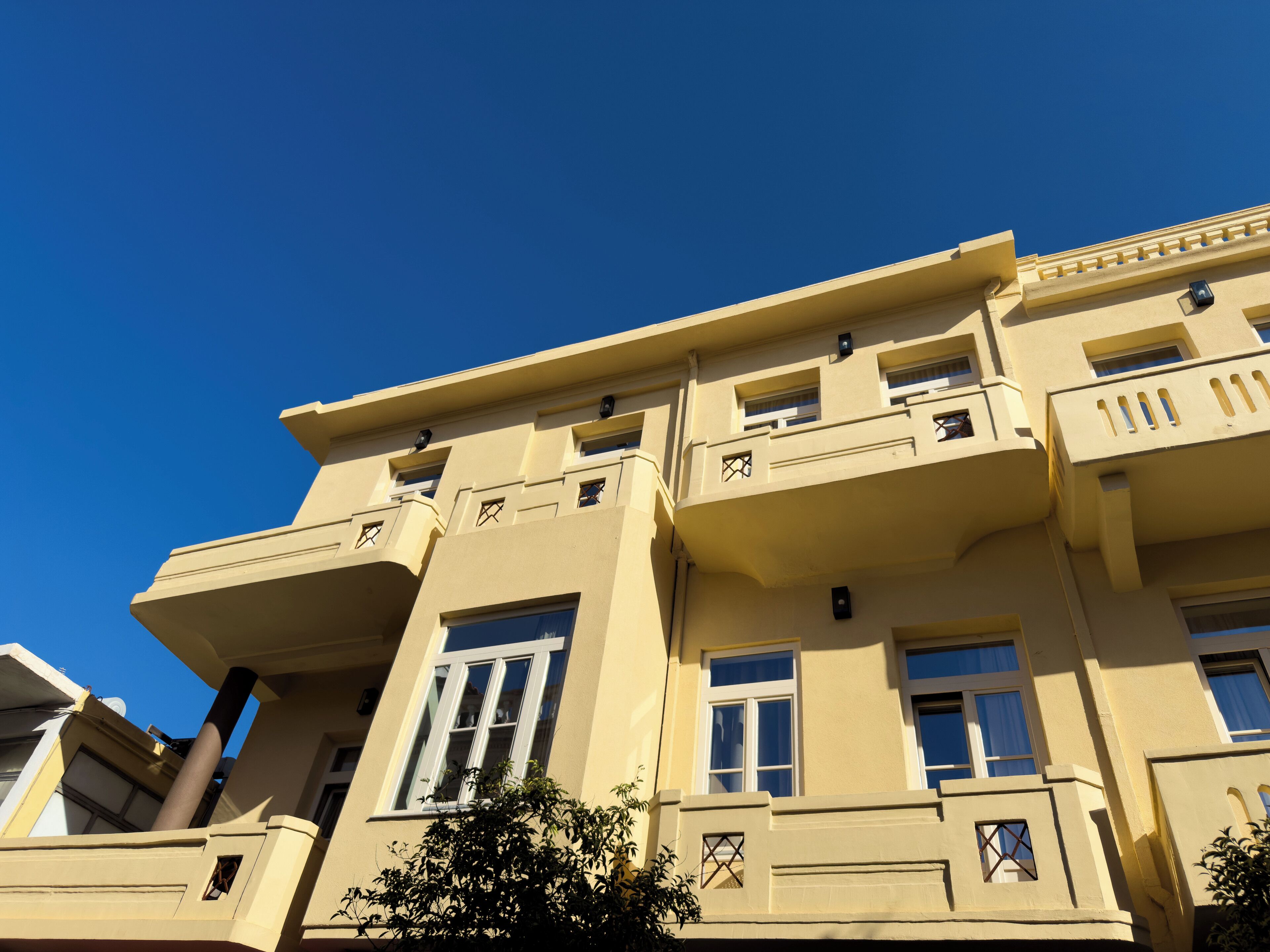 A multi-story building with balconies, large windows, and a clear blue sky.