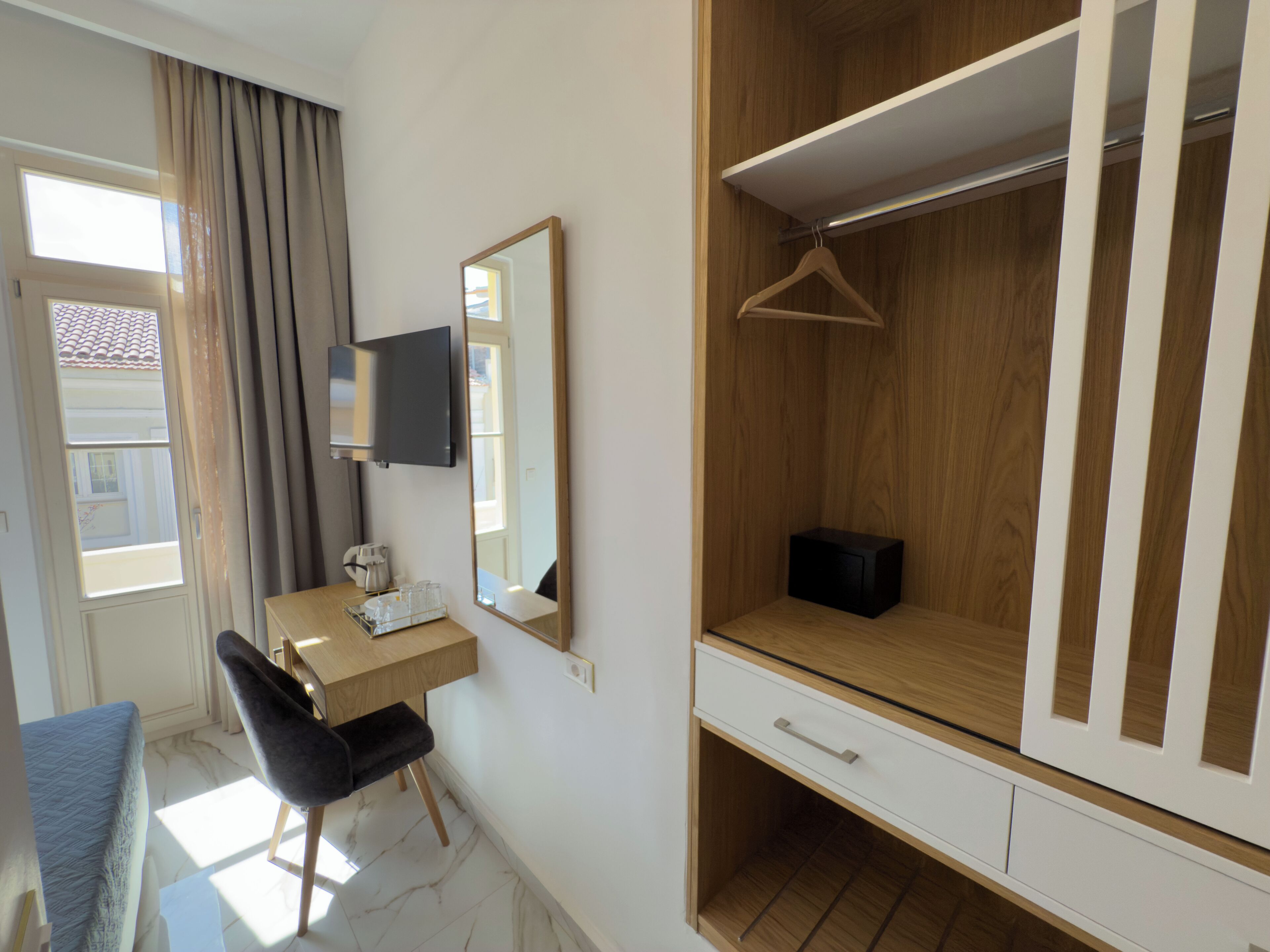 Habitación de hotel moderna con un armario de madera, un escritorio con silla, televisión y ventana con cortinas.