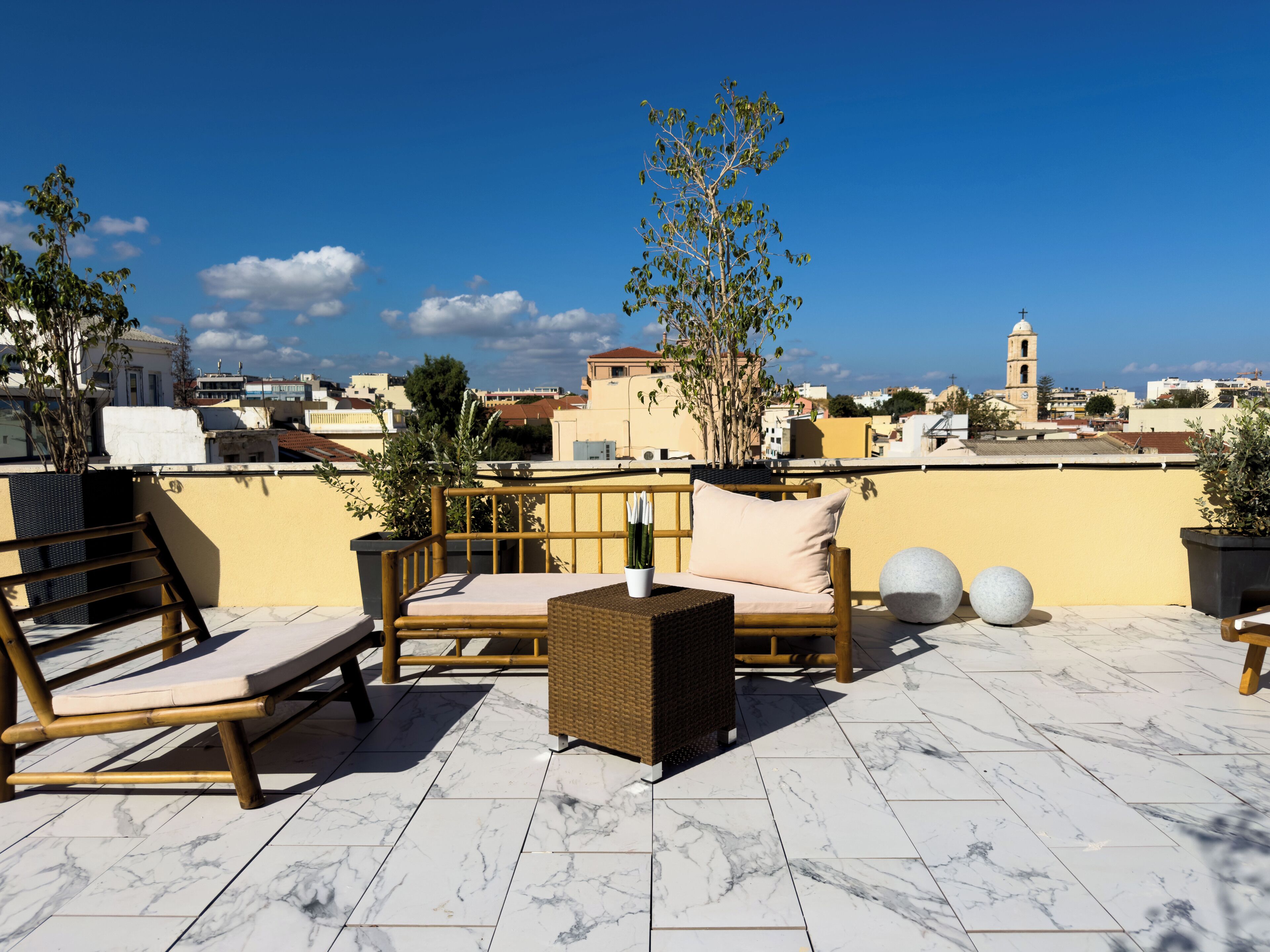 A rooftop terrace with a seating area, potted plants, and a view of the cityscape.