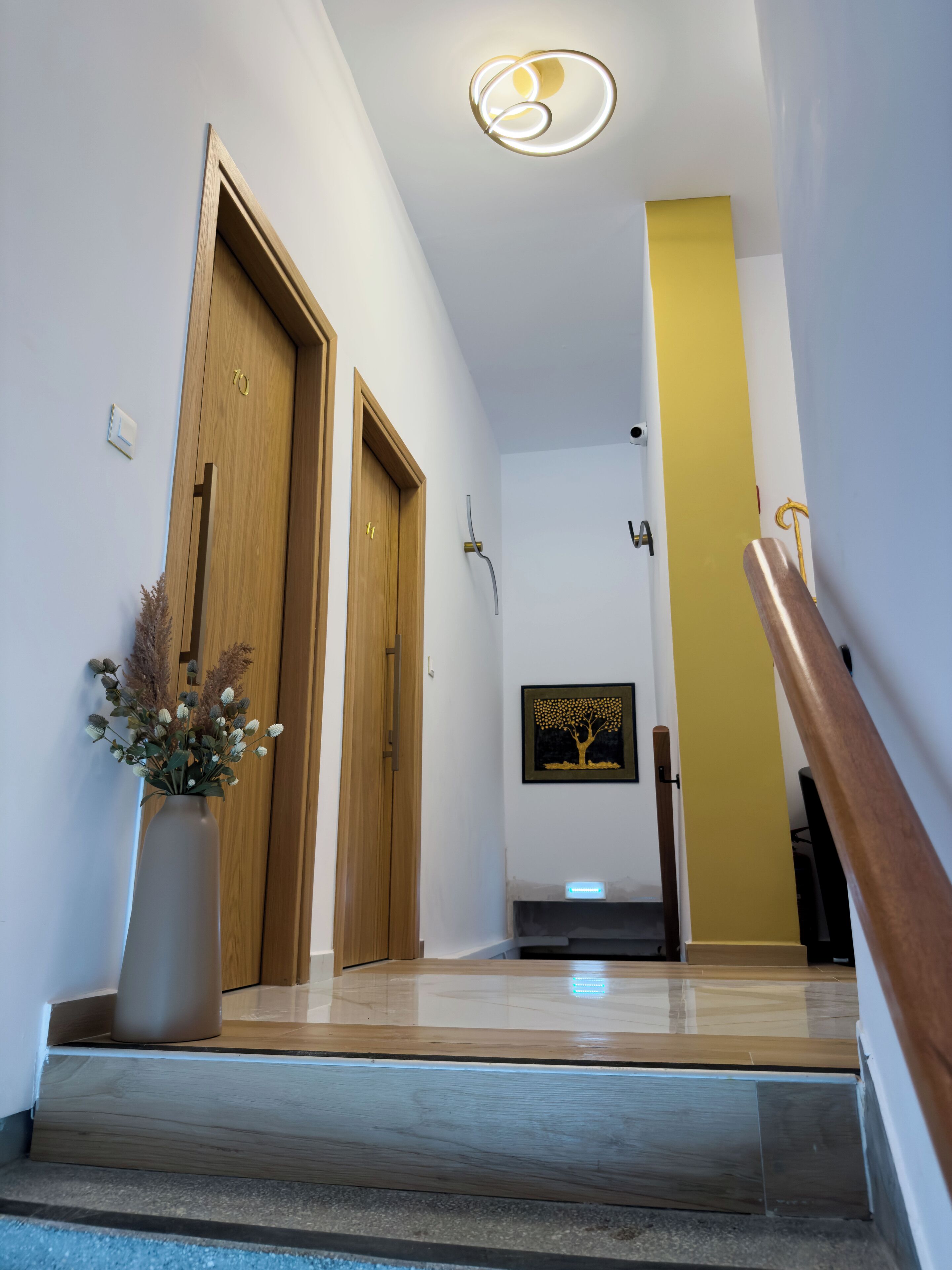 A modern hallway with wooden doors, a staircase, and a yellow accent wall.