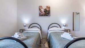 A hotel room with two single beds, each with a headboard, bedside tables, and lamps. There is a painting on the wall above the beds and a mirror on the wall to the right.