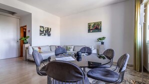 A modern living room with a sofa set, a dining table with chairs, and two wall-mounted paintings.
