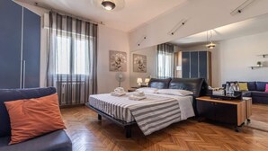 A modern hotel room with a bed, a sofa, a nightstand, and a mirror.