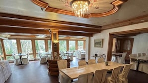 A spacious dining area with a large wooden table, white chairs, and a chandelier. - Gästehaus am Kurpark VS (Villingen-Schwenningen)
