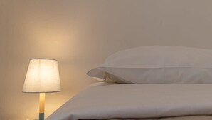 En seng med hvide sengetæpper og en lampe med hvid skærm på et natbord.