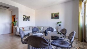 En moderne stue med et rundt glasbord, fire stole, en sofa og to billeder på væggen.