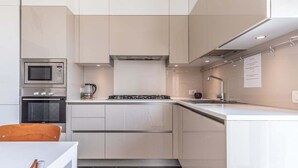 Une cuisine moderne avec des meubles blancs, un four encastré, un four à micro-ondes et une cuisinière à gaz.