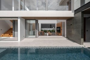 A modern house with a glass door entrance, a staircase, and a pool area.