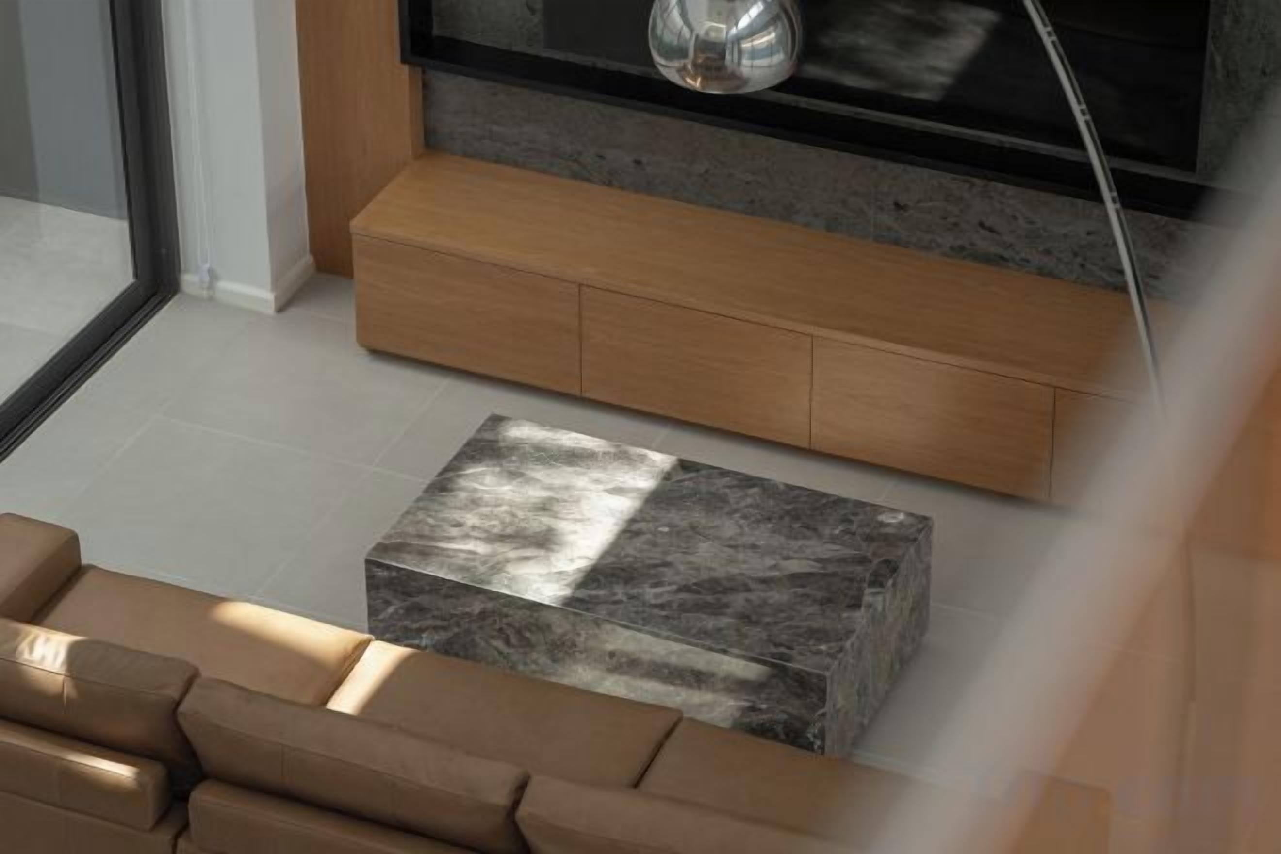 A modern living room with a sofa, a marble coffee table, and a built-in wooden cabinet.