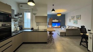A modern kitchen with a central island, a dining area with a wooden table, and a living room with a sofa and TV.