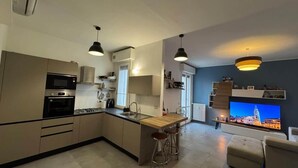 A modern kitchen with a central island, bar stools, a built-in oven, and a large TV screen displaying a cityscape.