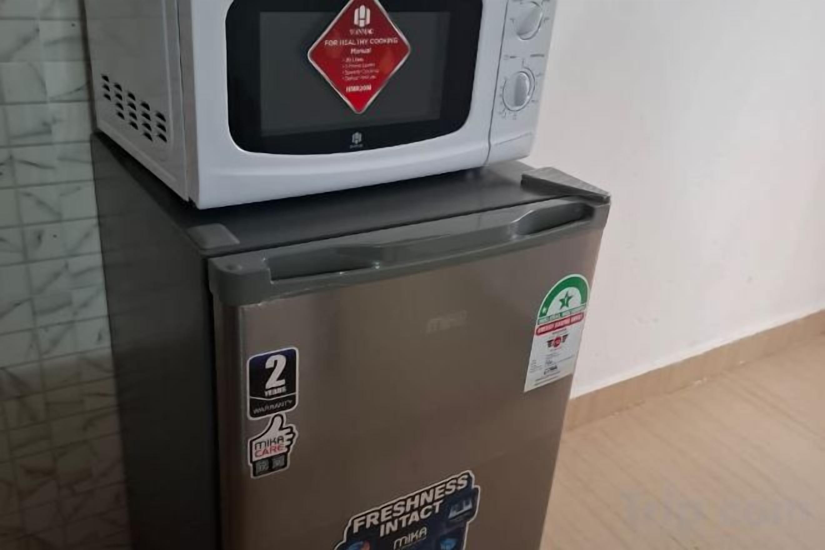 A refrigerator with a microwave on top, a sticker indicating 'freshness intact,' and a recycling symbol.