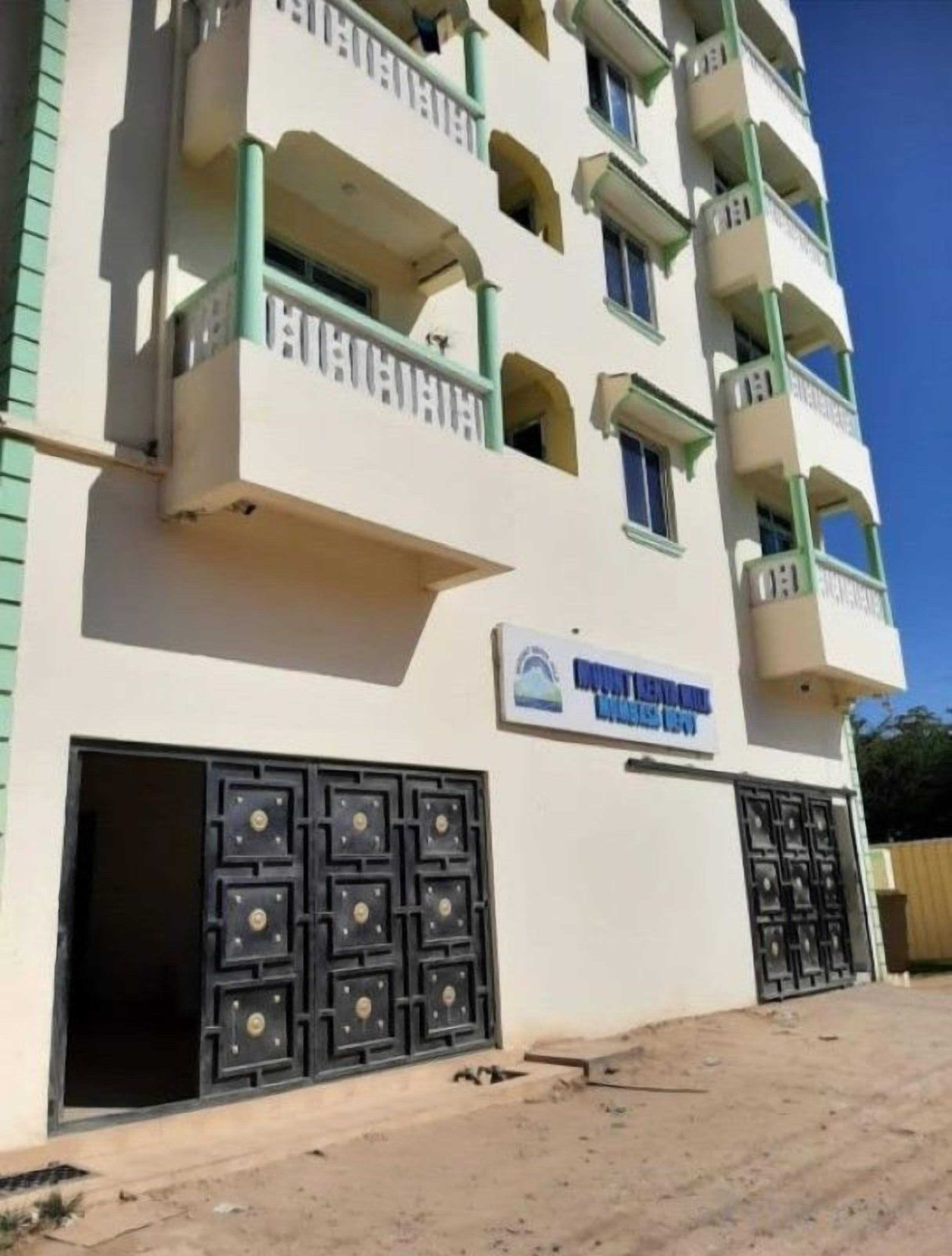A multi-story building with balconies, a sign indicating a business or commercial use, and a gated entrance.