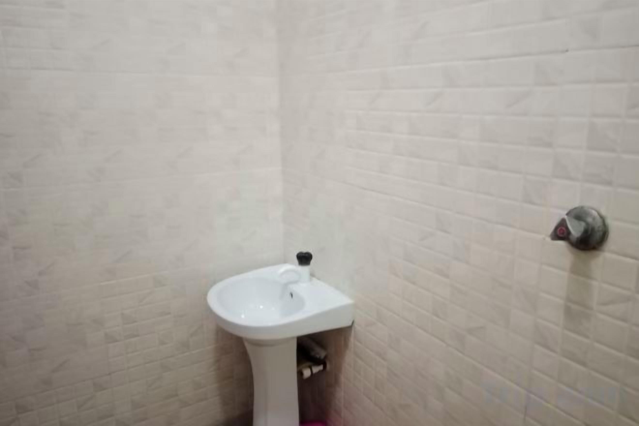 A bathroom with a white pedestal sink, tiled walls, and a wall-mounted faucet.