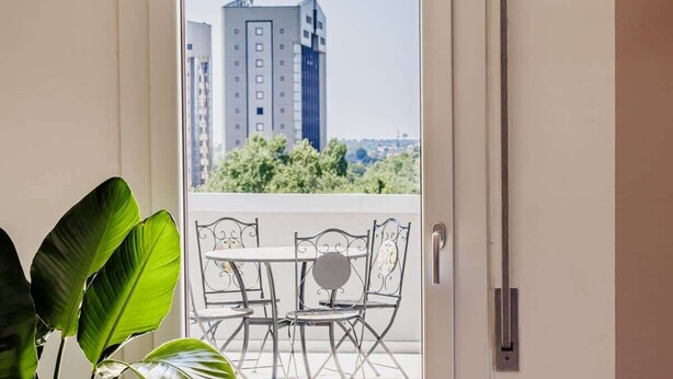 A balcony with a table and chairs, overlooking a cityscape with tall buildings and greenery. - Skyline Eighth Heaven - Affitti Brevi Italia (Modena)