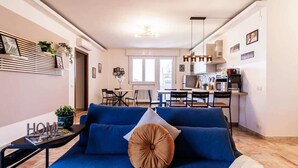A modern living room with a blue sofa, a small table with a magazine, and a kitchen in the background. - Skyline Eighth Heaven - Affitti Brevi Italia (Modena)