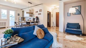 A modern living room with a blue sofa, a dining area with a table and chairs, and a kitchen in the background. - Skyline Eighth Heaven - Affitti Brevi Italia (Modena)